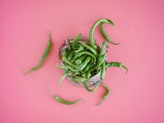 a heap of green chillies scattered on a pink surface overflowing from a paper bag