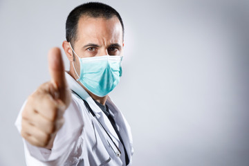 medico con camice bianco e mascherina chirurgica fa il segno di ok con il pollice verso su, isolato su sfondo bianco