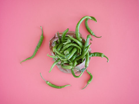 a heap of green chillies scattered on a pink surface overflowing from a paper bag