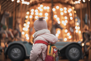 niña de espalda mirando un carroussel en invierno - obrazy, fototapety, plakaty