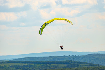 A man flying a green paraglider over a forest on a cloudy day.