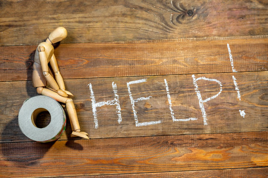 Wooden figure sit on a roll of toilet paper. Help inscription on wooden background. Concept of the problem with digestion.