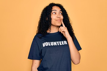 Young african american curly woman doing volunteering wearing volunteer t-shirt serious face...