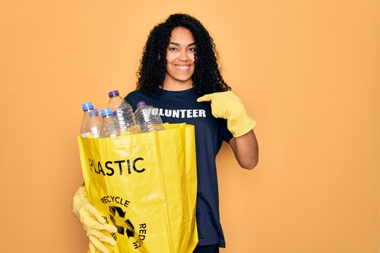 Young african american woman doing volunteering recycling holding bag with plastic bottles with surprise face pointing finger to himself