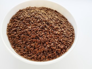 Flax seeds in a white ceramic plate on a white background.