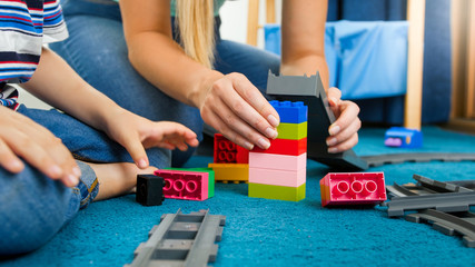 Closeup image of mother and son assembling toy bridge from colorful constructor bricks and blocks
