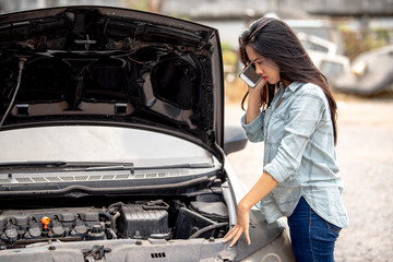 A beautiful Asian woman uses a smartphone to contact a broken car mechanic 