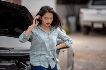A beautiful Asian woman uses a smartphone to contact a broken car mechanic 