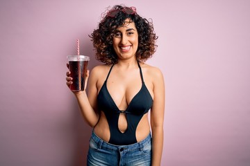 Beautiful arab woman on vacation wearing swimsuit drinking cola refreshment using straw with a happy face standing and smiling with a confident smile showing teeth