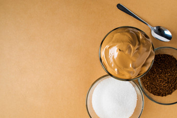 Dalgon's whipped coffee in a glass Cup on a white wooden background. Next to the ingredients for making a Korean refreshing coffee drink.