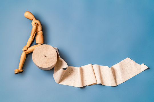 Wooden figure sit on a roll of toilet paper. Concept of the problem with digestion.