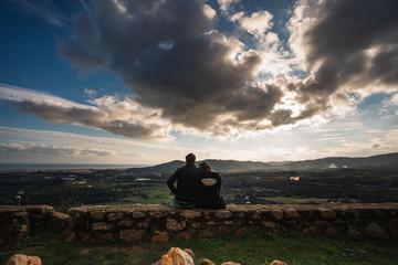 pareja abrazada mirando el atardecer desde la cima de una colina desde un castillo