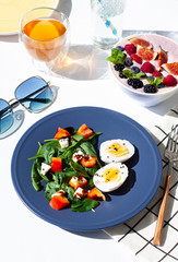 Healthy sunny morning breakfast on the white table. A Smoothie bowl and A Salad with spinach, red pepper, feta cheese eggs with boiled eggs. 