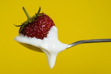 Macro shot of ripe strawberries on a spoon with sour cream. Closeup red berry with yellow background - 352600166