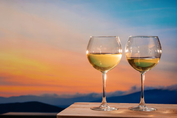 Romantic glass of wine sitting on the beach at colorful sunset. Glasses of white wine against sunset, white wine on the sky background with clouds - 352600535