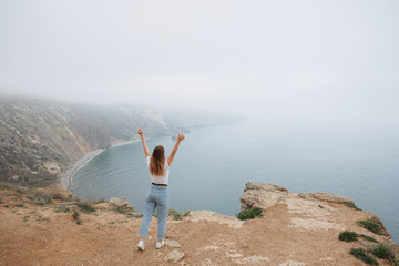 The girl went to the top of the mountain and admires the view of the Black Sea. Misty landscape from the cliff - 352600788