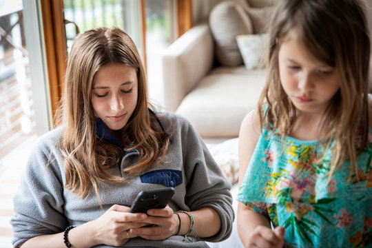 A teenager using her smart phone with her younger sister nearby