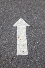 White arrow on cracked asphalt surface. Concept traffic.