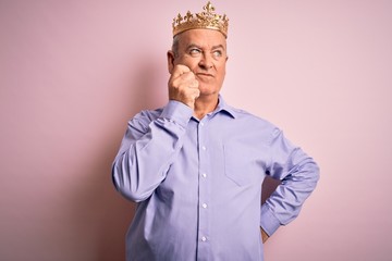 Middle age hoary man wearing golden crown of king standing over isolated pink background with hand on chin thinking about question, pensive expression. Smiling with thoughtful face. Doubt concept.