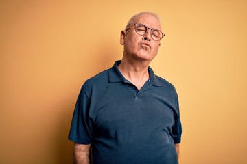 Middle age handsome hoary man wearing casual polo and glasses over yellow background looking at the camera blowing a kiss on air being lovely and sexy. Love expression.