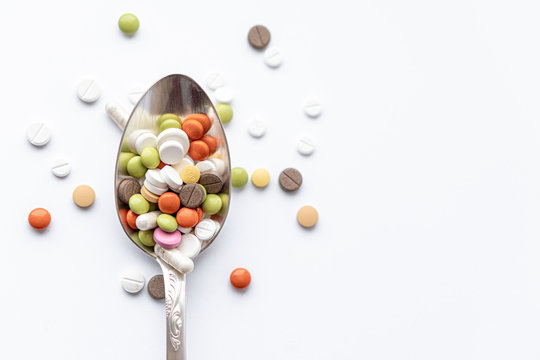 Medicine and health, treatment, pharmaceutics, coronavirus, pandemic, epidemic concept - layout one silver big tablespoon with multi-colored tablets and capsules on a white background copy space.