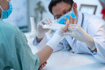 The doctor was wrapping the gauze closely with the patient by bandaging the man's hand (Focus on the hand).