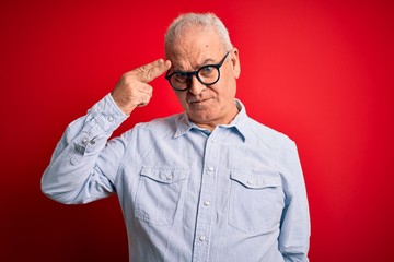 Middle age handsome hoary man wearing casual striped shirt and glasses over red background Shooting and killing oneself pointing hand and fingers to head like gun, suicide gesture.