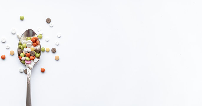 Medicine and health, treatment, pharmacy, coronavirus, pandemic, epidemic concept - banner layout one silver big tablespoon with multi-colored pills and capsules on a white background place for text.