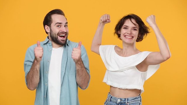 Young fun couple friends bearded guy girl in casual clothes posing isolated on yellow background studio. People emotions lifestyle concept. Look at camera smiling strong woman showing biceps muscles