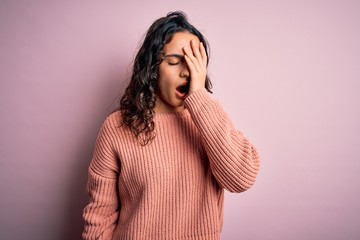 Young beautiful woman with curly hair wearing casual sweater over isolated pink background Yawning tired covering half face, eye and mouth with hand. Face hurts in pain.