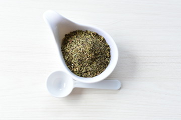 Chopped dried leaves of basil leaves on white wooden background