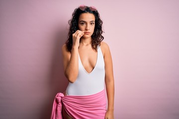 Beautiful woman with curly hair on vacation wearing white swimsuit over pink background mouth and...