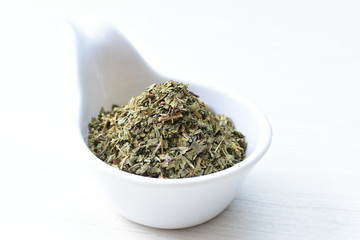 Chopped dried leaves of basil leaves on white wooden background