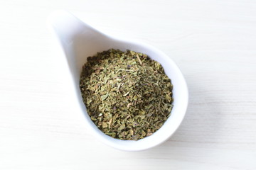 Chopped dried leaves of basil leaves on white wooden background