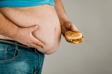 fat man with a hamburger in his hand on a gray background.