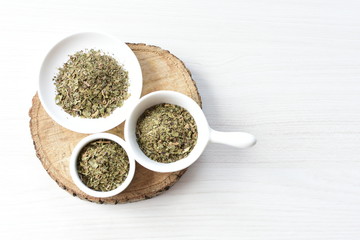 Chopped dried leaves of basil leaves on white wooden background