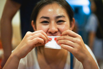 Young happy smiling Asian girl wipes mouth after eating food at the restaurant, white tissue, good manner at the table, happiness, selective focus, blurred bokeh, dark film noise grain
