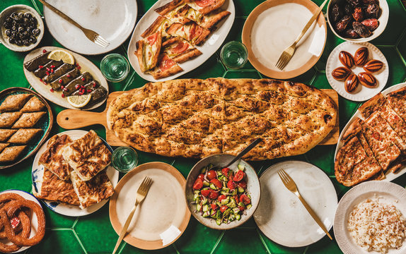 Muslim Ramadan iftar family dinner. Flat-lay of Middle East food table with dates, dolma, kebab, flatbread, pide, borek, sweets, salad, top view, copy space. Ramazan fasting Turkish cuisine