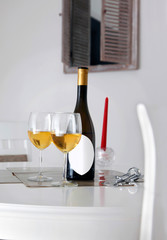 Bottle of wine with white label for caption, opener, two glasses of white wine on table and window in background