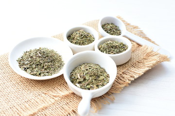 Chopped dried leaves of basil leaves on white wooden background