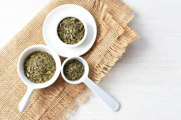 Chopped dried leaves of basil leaves on white wooden background