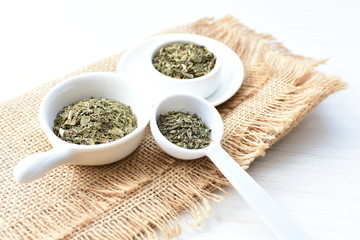 Chopped dried leaves of basil leaves on white wooden background