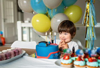 Little three years old boy making wish looking at candles on his birthday cake at home with...