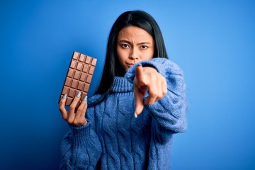 Fototapeta na wymiar Young beautiful chinese woman holding chocolate bar over isolated blue background pointing with finger to the camera and to you, hand sign, positive and confident gesture from the front