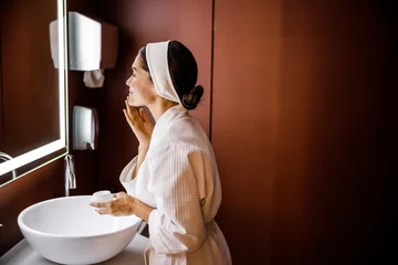 Fotobehang Badkamer Happy female applying face cream in bathroom  © Yakobchuk Olena
