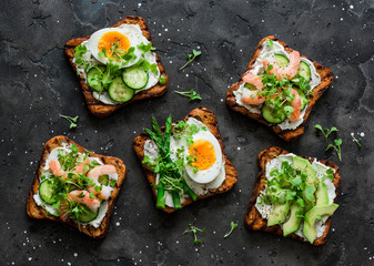 Variety sandwiches with cream cheese, egg, asparagus, avocado, cucumber, shrimp, micro greens on a dark background, top view