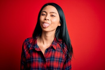 Young beautiful chinese woman wearing casual shirt over isolated red background sticking tongue out happy with funny expression. Emotion concept.