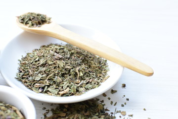 Chopped dried leaves of basil leaves on white wooden background