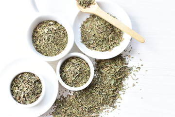Chopped dried leaves of basil leaves on white wooden background