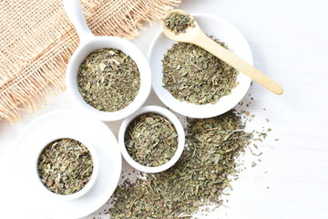 Chopped dried leaves of basil leaves on white wooden background